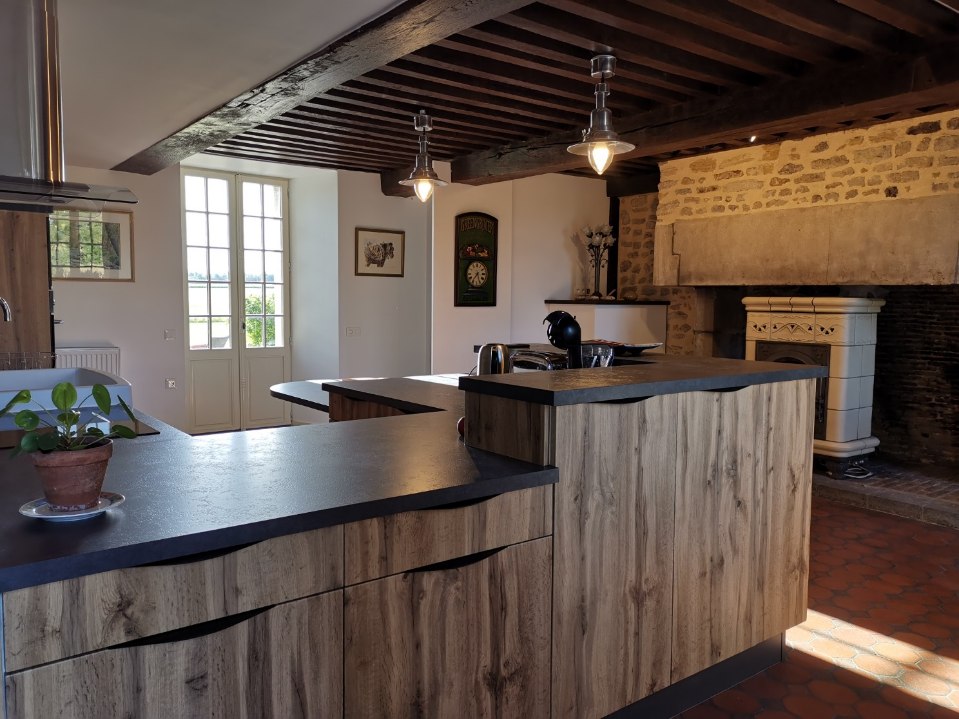 Cuisine rustique avec poutres apparentes, cheminée ancienne et îlot central en bois massif.